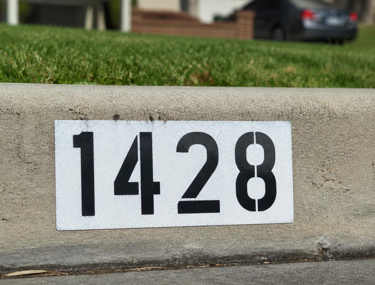 Freshly painted black house numbers on a white background stenciled onto a residential curb
